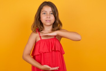 young Caucasian girl standing against yellow background gesturing with hands showing big and large size sign, measure symbol. Smiling looking at the camera. Measuring concept.