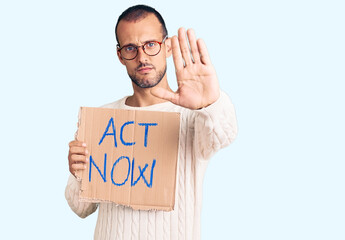 Young handsome man holding act now banner with open hand doing stop sign with serious and confident expression, defense gesture
