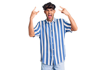 Young hispanic man wearing casual clothes shouting with crazy expression doing rock symbol with hands up. music star. heavy music concept.