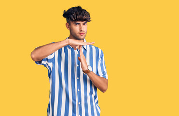 Young hispanic man wearing casual clothes doing time out gesture with hands, frustrated and serious...