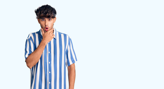 Young hispanic man wearing casual clothes looking fascinated with disbelief, surprise and amazed expression with hands on chin