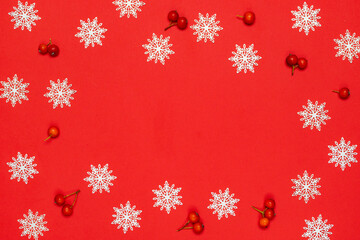 Xmas pattern. White snowflakes, red berry in Christmas composition on red background for greeting card. Flat lay, top view, copy space.