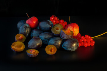 Bright autumn composition of blue plums, red apples and viburnum branches on a black background. Layout for autumn offers. Studio light. Horizontal arrangement.
