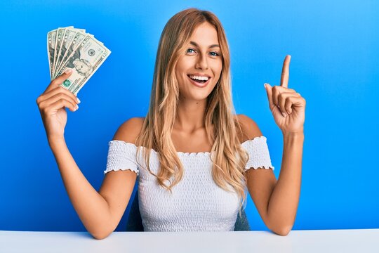 Beautiful blonde young woman holding 20 dollars banknotes smiling happy pointing with hand and finger to the side