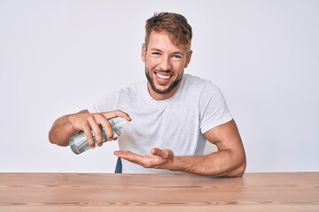 Young caucasian man using hand sanitizer gel sitting on the table smiling and laughing hard out loud because funny crazy joke.
