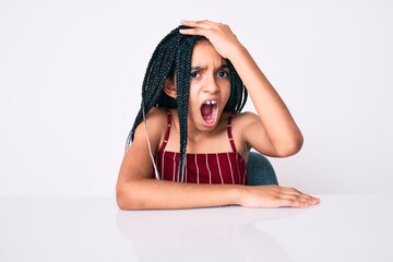 Young african american girl child with braids wearing casual clothes sitting on the table surprised...