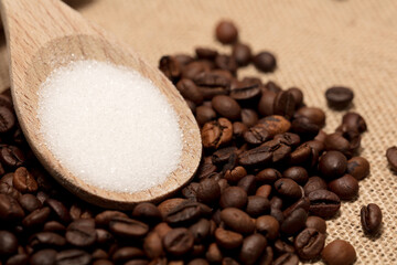 sugar in a wooden spoon, coffee beans and
raffia fabric background
