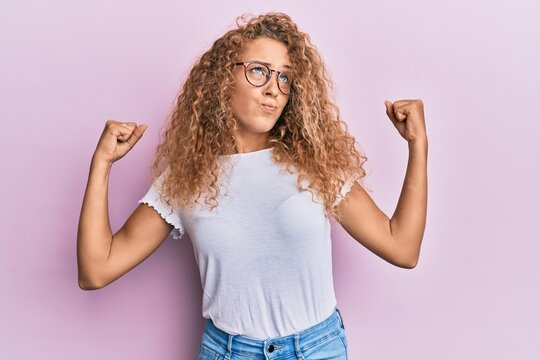 Beautiful caucasian teenager girl wearing white t-shirt over pink background showing arms muscles smiling proud. fitness concept.