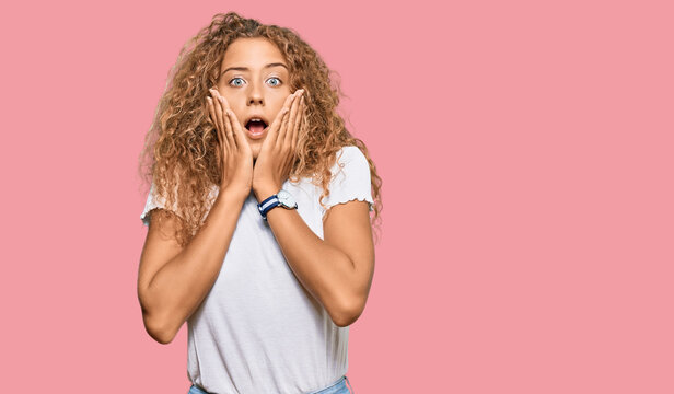 Beautiful caucasian teenager girl wearing casual white tshirt afraid and shocked, surprise and amazed expression with hands on face