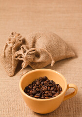 yellow coffee cup with beans and raffia cloth sacks, brown background