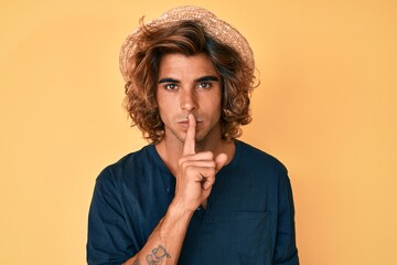 Young hispanic man wearing summer hat asking to be quiet with finger on lips. silence and secret...