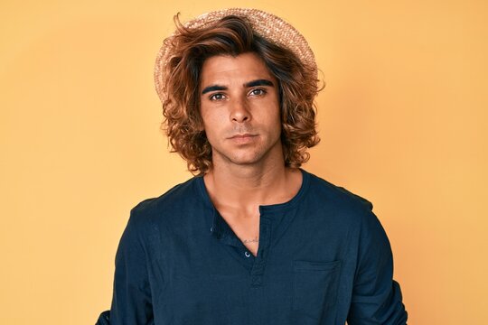 Young hispanic man wearing summer hat relaxed with serious expression on face. simple and natural looking at the camera.