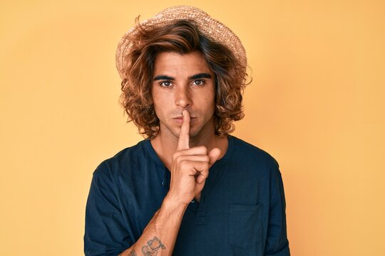 Young hispanic man wearing summer hat asking to be quiet with finger on lips. silence and secret concept.