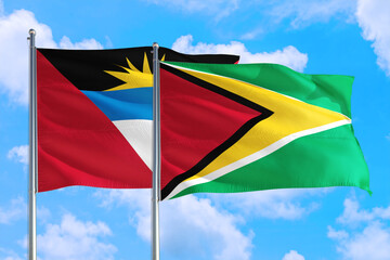 Fototapeta na wymiar Guyana and Antigua and Barbuda national flag waving in the windy deep blue sky. Diplomacy and international relations concept.