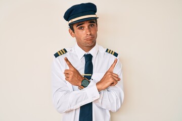 Young hispanic man wearing airplane pilot uniform pointing to both sides with fingers, different direction disagree