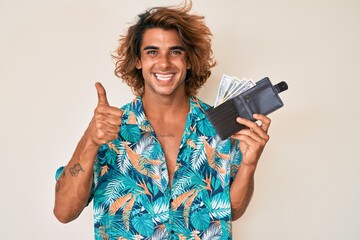 Young hispanic man holding leather wallet smiling happy and positive, thumb up doing excellent and approval sign