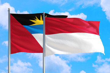 Indonesia and Antigua and Barbuda national flag waving in the windy deep blue sky. Diplomacy and international relations concept.