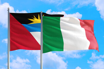 Italy and Antigua and Barbuda national flag waving in the windy deep blue sky. Diplomacy and international relations concept.