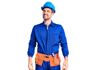 Young handsome man wearing worker uniform and hardhat looking away to side with smile on face, natural expression. laughing confident.