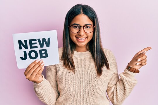 Young latin girl holding new job message on paper smiling happy pointing with hand and finger to the side
