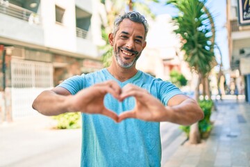 Middle age grey-haired man wearing casual clothes at street of city smiling in love showing heart symbol and shape with hands. romantic concept.