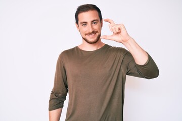 Young handsome man wearing casual clothes smiling and confident gesturing with hand doing small size sign with fingers looking and the camera. measure concept.