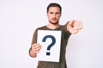 Young handsome man holding question mark pointing with finger to the camera and to you, confident gesture looking serious