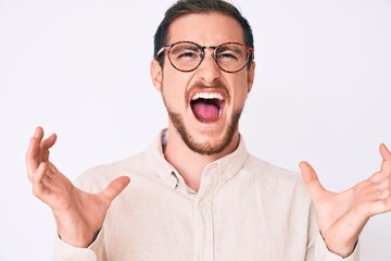 Young handsome man wearing casual clothes and glasses crazy and mad shouting and yelling with aggressive expression and arms raised. frustration concept.