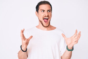 Fototapeta premium Young handsome man wearing casual white tshirt crazy and mad shouting and yelling with aggressive expression and arms raised. frustration concept.