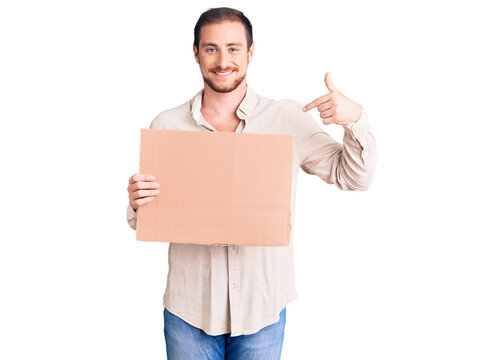 Young handsome caucasian man holding empty cardboard banner pointing finger to one self smiling happy and proud