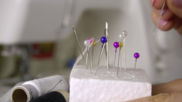 The seamstress sticks needles and pins with colored heads into the foam. Fingers and pins close up.Equipment for sewing.