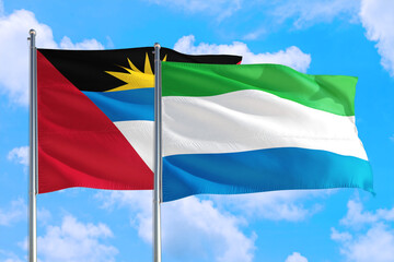 Sierra Leone and Antigua and Barbuda national flag waving in the windy deep blue sky. Diplomacy and international relations concept.