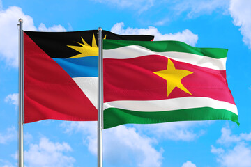 Suriname and Antigua and Barbuda national flag waving in the windy deep blue sky. Diplomacy and international relations concept.