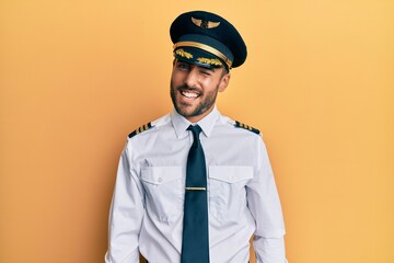 Handsome hispanic man wearing airplane pilot uniform winking looking at the camera with sexy expression, cheerful and happy face. © Krakenimages.com