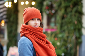 Portrait of a girl in a red hat and scarf, a walk through the Christmas city, a smile on her face, cool weather, a fascinating look