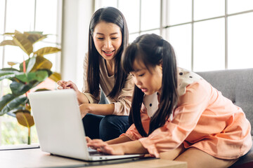 Mother and asian kid little girl learning and looking at laptop computer making homework studying knowledge with online education e-learning system.children video conference with teacher tutor at home