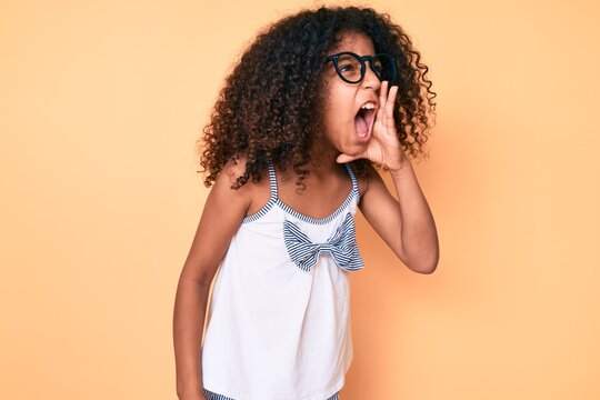 African american child with curly hair wearing casual clothes and glasses shouting and screaming loud to side with hand on mouth. communication concept.