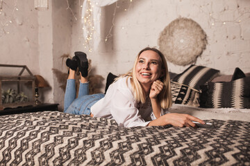 Happy young woman lies on the bed on Christmas eve and speaks on the phone. Woman in gray sweater,...