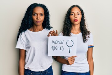 African american mother and daughter holding women rights banner thinking attitude and sober expression looking self confident