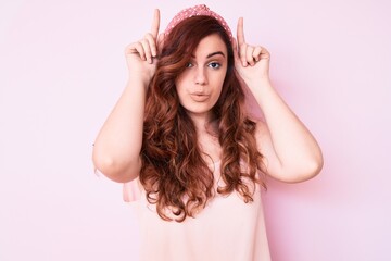 Young beautiful woman wearing casual clothes doing funny gesture with finger over head as bull horns