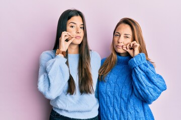 Hispanic family of mother and daughter wearing wool winter sweater mouth and lips shut as zip with...