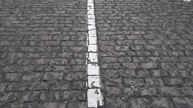 Ancient stone paving road in old town. Cobblestone pavement with damaged white single line road marking in center of frame. Roman road texture. Camera moves tilt