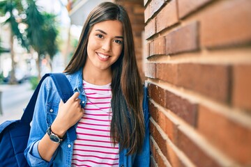 Young hispanic student girl smiling happy leaning on the wall at the city.