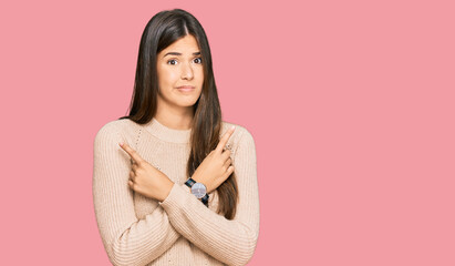 Fototapeta premium Young brunette woman wearing casual winter sweater pointing to both sides with fingers, different direction disagree