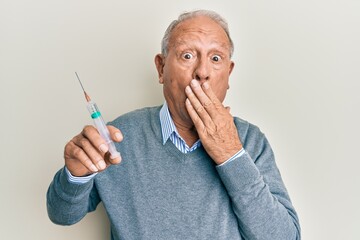 Senior caucasian man holding syringe covering mouth with hand, shocked and afraid for mistake....