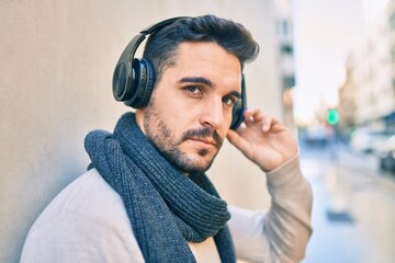 Young hispanic man with relaxed expression listening to music using headphones at the city.
