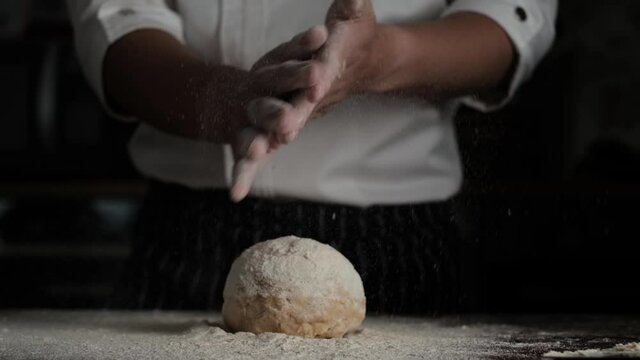 Slow Motion shot of  bakery chef applying flour on hands and clapping before making bread dough. Baking concept.