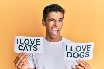 Young handsome african american man holding paper with i love cats and i love dogs phrase winking looking at the camera with sexy expression, cheerful and happy face.