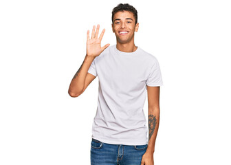 Young handsome african american man wearing casual white tshirt showing and pointing up with fingers number five while smiling confident and happy.