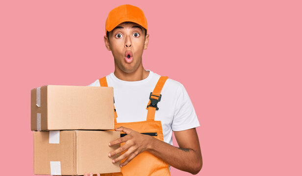 Young handsome african american man holding delivery package scared and amazed with open mouth for surprise, disbelief face